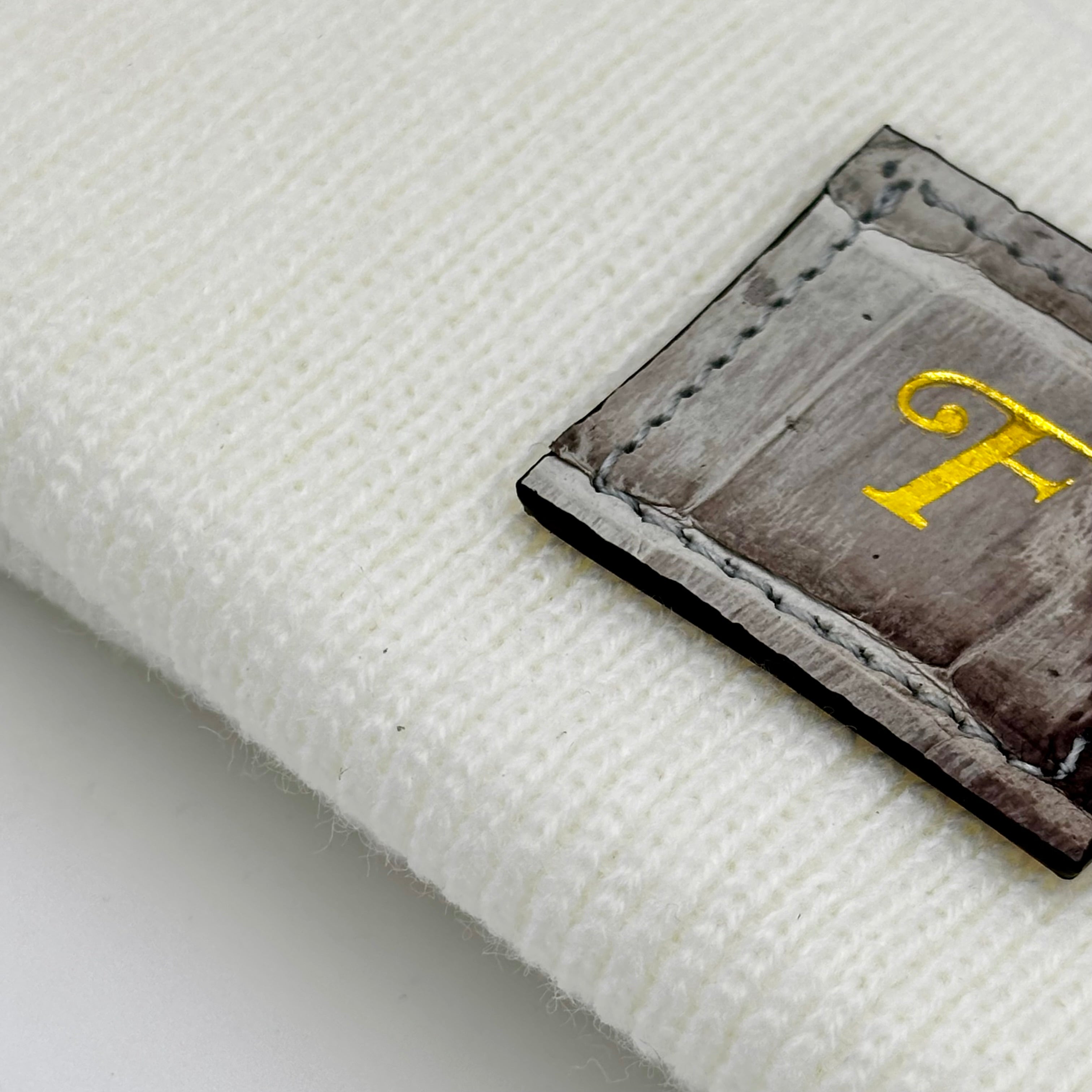 Close-up of Himalayan alligator leather patch with gold Frostytch monogram on white knit beanie