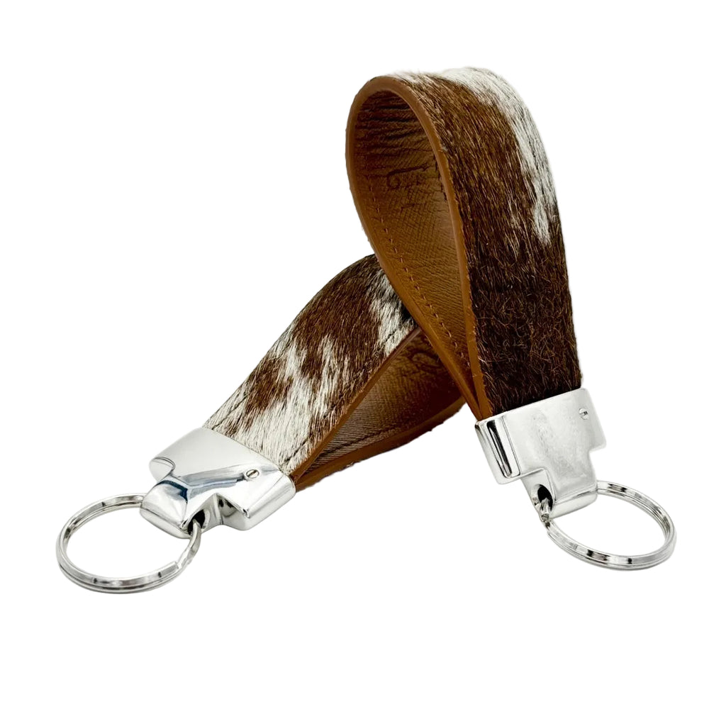 Two brown-and-white cowhide key fobs showing leather-lined loops and silver split key rings